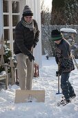 Mann schiebt Schnee mit Schneeschaufel auf der Terrasse