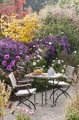 Autumnal gravel terrasse with small seating group on the flowerbed with aster