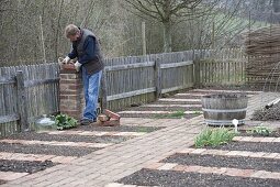 Mann legt Weg aus Klinker und mauert Verkleidung für Wasserleitung