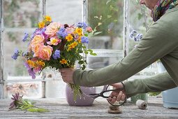 Frau bindet Strauss aus Rosa (Rosen), Cosmos (Schmuckkörbchen)