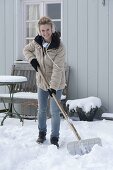 Frau schippt Schnee auf der Terrasse