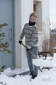 Frau schippt Schnee auf der Terrasse