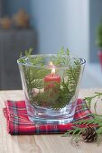 Glas mit roter Kerze als Windlicht, dekoriert mit Thuja (Lebensbaum)