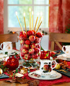 Tischdekoration mit Apfelgeschirr, Glasgefäß mit Äpfeln gefüllt, Laub, Windlicht