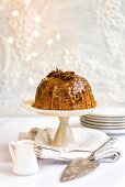Steamed ginger and date pudding drizzled with toffee sauce and decorated with star anise on a cake stand