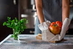 Frau hält eine Fleischtomate (Zutat für Cocido madrileno - Eintopf aus Spanien)