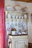 Wandregal mit weißem Geschirr und alter Backschrank mit Küchenutensilien