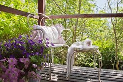Vintage-style crockery on ornate metal table and cushion on chair on wooden deck