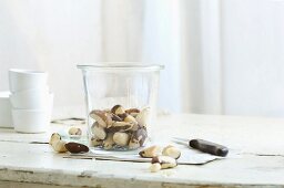 Brazil nuts in and next to a glass jar on a rustic kitchen table