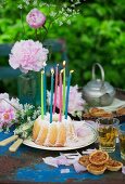 A garden table with peonies, a 'Gugelhupf' ring cake with candles and springtime herb tea