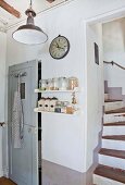 Staircase next to kitchen shelves and grey wooden door in country house