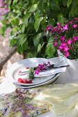 Blades of grass and scented pinks wrapped around napkin and cutlery on plate