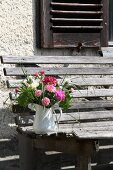 Posies of carnations in jug on weathered garden bench