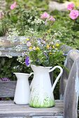 Bemalte Krugvase mit Wiesenblumenstrauß auf Vintage Gartenbank