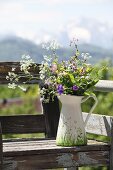Wild flowers in white, painted jug on vintage garden bench