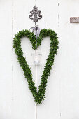 Candle lantern in heart-shaped box wreath hung on white wooden door