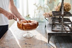 Hands of man cutting slice of pound cake on cake stand