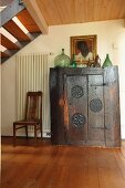 Collection of bottles on top of ornate, antique, ethnic wooden cabinet below staircase