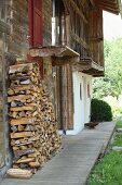 Brennholzstapel vor verwitterter Holzfassade
