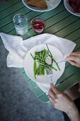 Frau isst blanchierten grünen Spargel (Draufsicht)