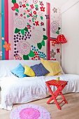 White throw and scatter cushions on couch in front of colourful wall decorated with large floral motifs