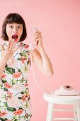 A young brunette woman wearing a floral dress and holding a telephone receiver in her hand