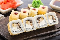 Sushi rolls with smoked eel and banana on a wooden board