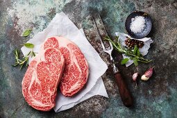 Rohes Ribeye Steak vom Angusrind, Gewürze und Fleischgabel auf Metalluntergrund