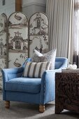 Blue armchair with beige scatter cushions in front of upholstered screen