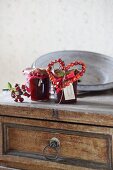 Jars of jam decorated with rose-hip love-heart on top of vintage chest of drawers