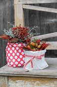 Autumn arrangements of rose hips and autumn leaves in pots wrapped in gift wrap on vintage wooden bench