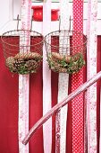 Various pine cones and box sprigs in vintage wire baskets and strips of fabric hung from window frame