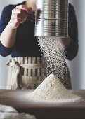 Frau siebt Mehl fürs Backen mit Mehlsieb auf Arbeitsplatte