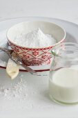 A bowl of icing sugar and a glass of milk for making icing