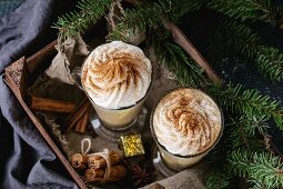 Pumpkin spicy latte with whipped cream and cinnamon in two glasses standing in wooden board with Christmas decoration