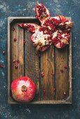 Fresh ripe pomegranates cut in pieces in rustic wooden tray