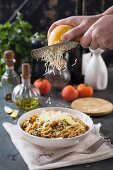 Cheese grated over spaghetti with tomato sauce and herbs