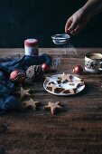 Woman dusting almonds cinnamon Christmas cookies with powdered sugar on a plate and rustic wooden table