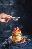 Puderzucker wird auf einen Stapel Hafermehl-Pancakes mit Erdbeeren und Ahornsirup gestäubt