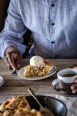 A man is served a slice of caramel apple pie topped with a scoop of vanilla bean ice cream