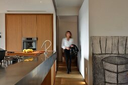 Offene Designerküche aus Holz mit Metalltheke, Frau im Durchgang