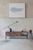 Schlichtes Lowboard aus wiederverwendetem Holz mit schwarzer Tischleuchte vor gerahmtem Kunstobjekt