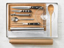 Various kitchen utensils: baking tray, knife, peeler, meat fork, baking paper