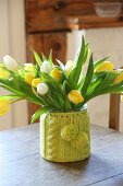 Tulips in vase with knitted cover on old wooden table