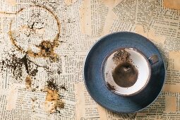 Blue ceramic cup of coffee grounds over old newspaper