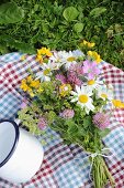 Checked picnic blanket, posy of wildflowers and white enamel mug on lawn
