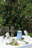 Gedeckter Gartentisch mit buntem Wiesenblumenstrauss und hellblauer Emaillekanne
