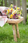 Bunter Wiesenblumenstrauss auf Vintage Holzschemel im Grünen