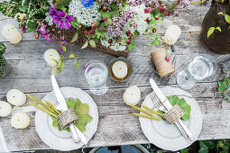 Gedeckter Tisch mit Wiesenblumen, Kerzen und Blättern