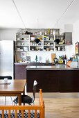 Open-fronted shelves and U-shaped base units in kitchen with dining area in foreground